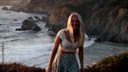 Handheld sunset shot of blonde walking away from beach with waves in background
