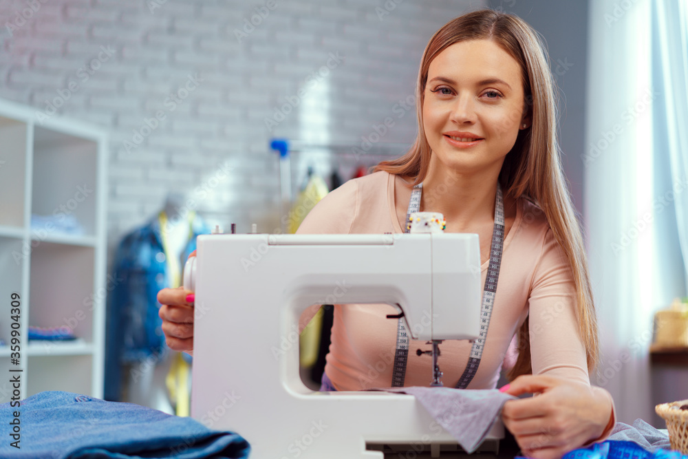 Cheerful young seamstress sitting at working table in her office