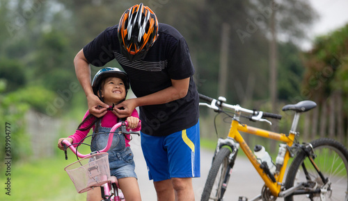 Canvas Print Happy father and daughter cycling in the park wears a bicycle helmet to his daug