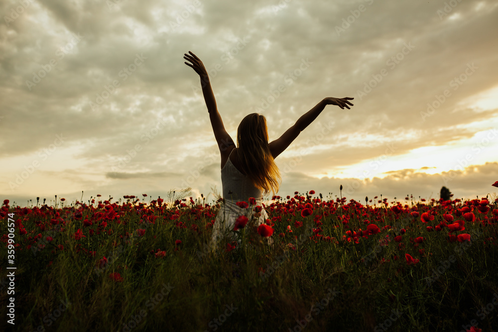 Silhouette of woman who stands toward the amazing sunset in a red poppy ...