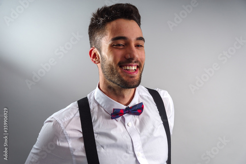 Leinwand Poster Young model in white shirt, suspenders, bow tie, piercings and fledgling beard