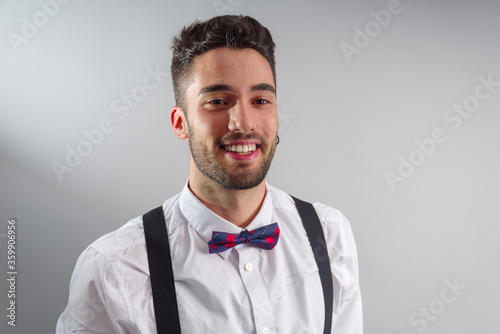 Young model in white shirt, suspenders, bow tie, piercings and fledgling beard