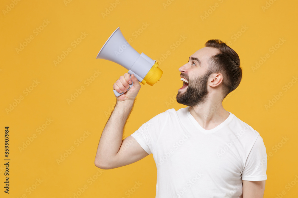 Excited young bearded man guy in white casual t-shirt posing isolated on yellow background studio portrait. People emotions lifestyle concept. Mock up copy space. Scream in megaphone looking aside up. Excited young bearded man guy in white casual t-shirt posing isolated on yellow background studio portrait. People emotions lifestyle concept. Mock up copy space. Scream in megaphone looking aside up.