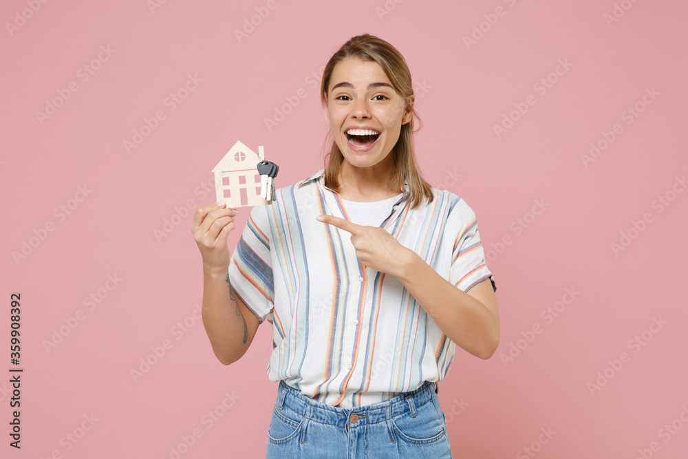 Excited young blonde woman girl in casual striped shirt posing isolated on pastel pink background studio. People lifestyle concept. Mock up copy space. Pointing index finger on house, bunch of keys. Excited young blonde woman girl in casual striped shirt posing isolated on pastel pink background studio. People lifestyle concept. Mock up copy space. Pointing index finger on house, bunch of keys.