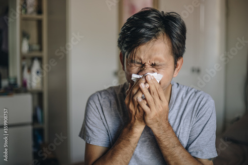 Young Asian man is sick covering his mouth with tissue in bedroom.