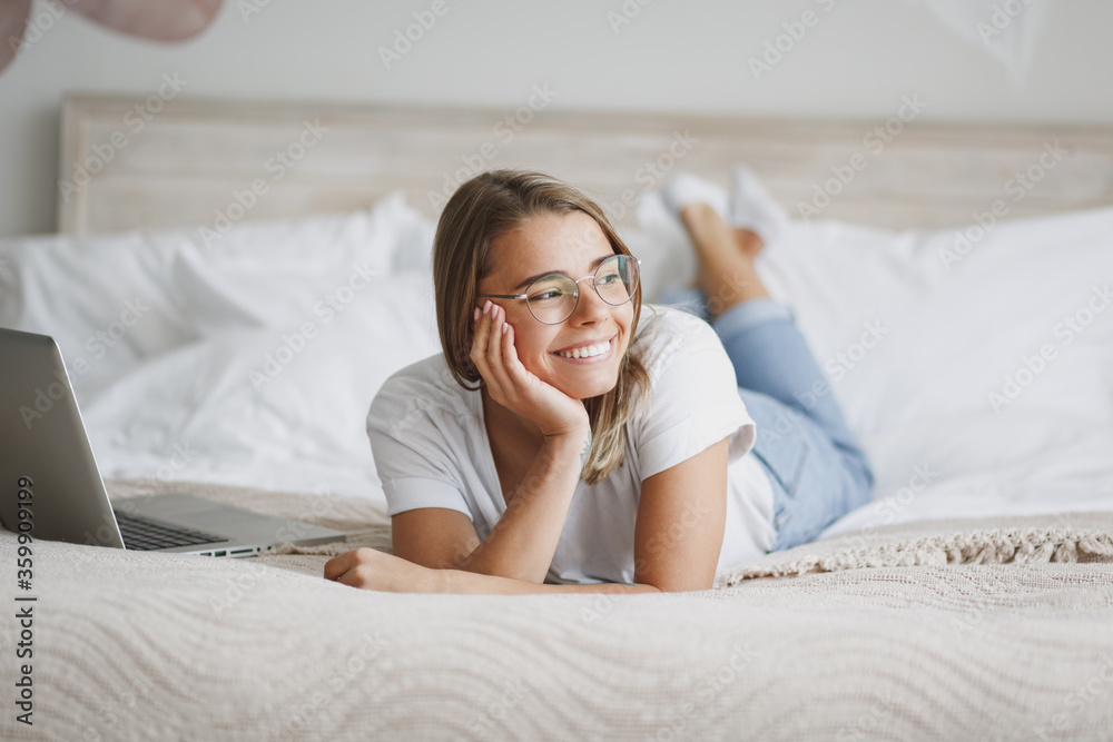 Beautiful young woman girl in white t-shirt glasses lying in bed with white sheet pillow blanket spending time in bedroom at home. Rest relax good mood lifestyle concept. Put hand prop up on cheek. Beautiful young woman girl in white t-shirt glasses lying in bed with white sheet pillow blanket spending time in bedroom at home. Rest relax good mood lifestyle concept. Put hand prop up on cheek.
