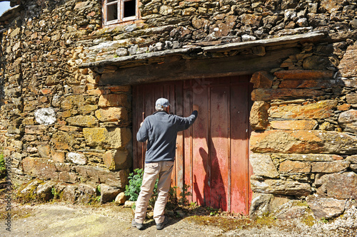 Hombre llamando en la puerta de una casa en el pueblo de As Eiras en el Camino de Santiago a Laza, provincia de Orense, España