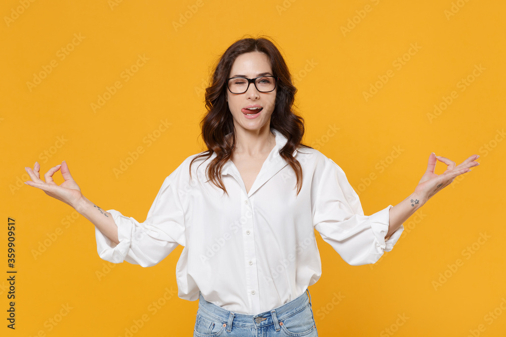 Blinking young brunette business woman in white shirt glasses isolated on yellow background. Achievement career wealth business concept. Hold hands in yoga gesture, relaxing meditating showing tongue. Blinking young brunette business woman in white shirt glasses isolated on yellow background. Achievement career wealth business concept. Hold hands in yoga gesture, relaxing meditating showing tongue.