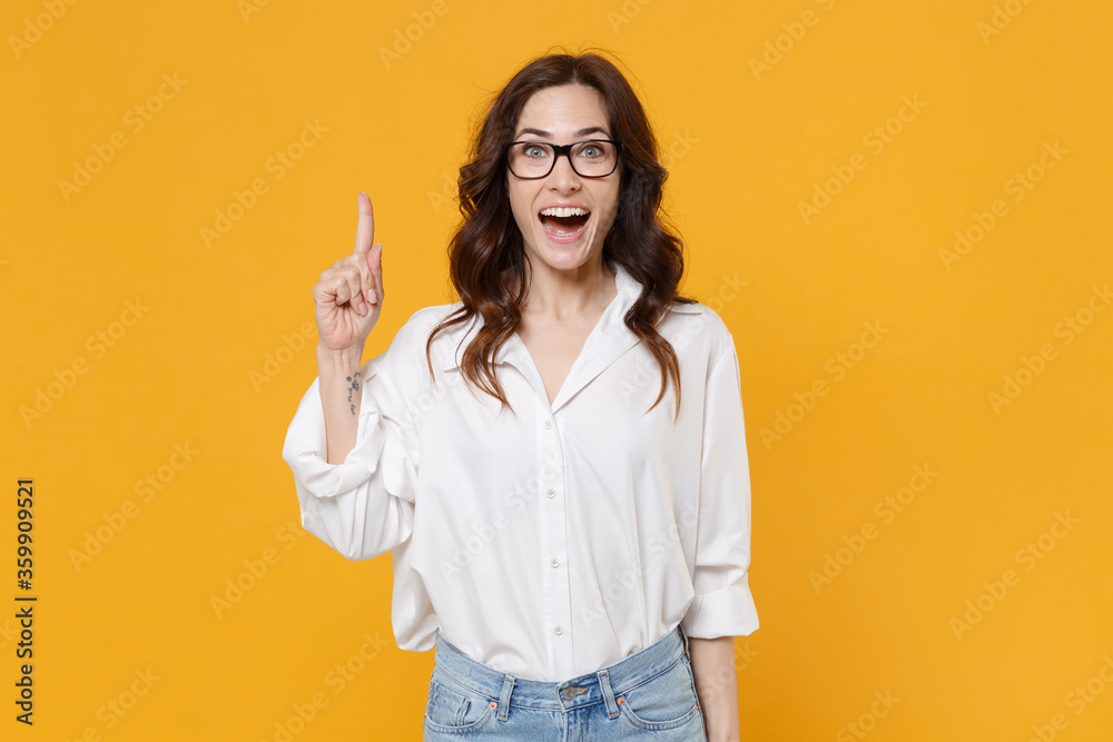 Excited young business woman in white shirt glasses isolated on yellow background studio. Achievement career wealth business concept. Mock up copy space. Holding index finger up with great new idea. Excited young business woman in white shirt glasses isolated on yellow background studio. Achievement career wealth business concept. Mock up copy space. Holding index finger up with great new idea.