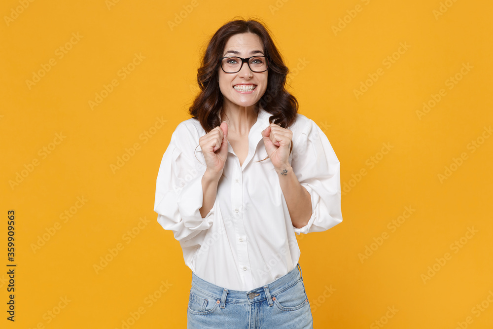 Excited young business woman in white shirt glasses isolated on yellow background. Achievement career wealth business concept. Mock up copy space. Clenching fists, making wish wait for special moment. Excited young business woman in white shirt glasses isolated on yellow background. Achievement career wealth business concept. Mock up copy space. Clenching fists, making wish wait for special moment.