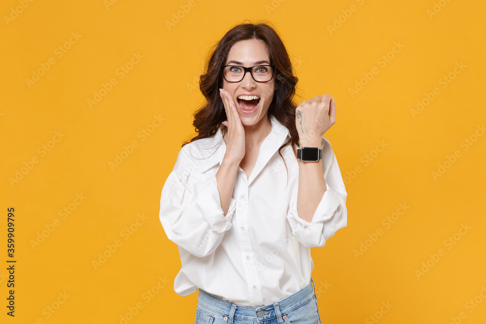 Excited brunette business woman in white shirt glasses isolated on yellow background. Achievement career wealth business concept. Mock up copy space. Wearing smart watch on hand, put hand on cheek. Excited brunette business woman in white shirt glasses isolated on yellow background. Achievement career wealth business concept. Mock up copy space. Wearing smart watch on hand, put hand on cheek.