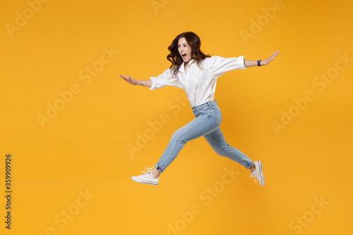 Side view excited young brunette business woman in white shirt posing isolated on yellow background. Achievement career wealth business concept. Mock up copy space. Jumping  spreading hands and legs.
