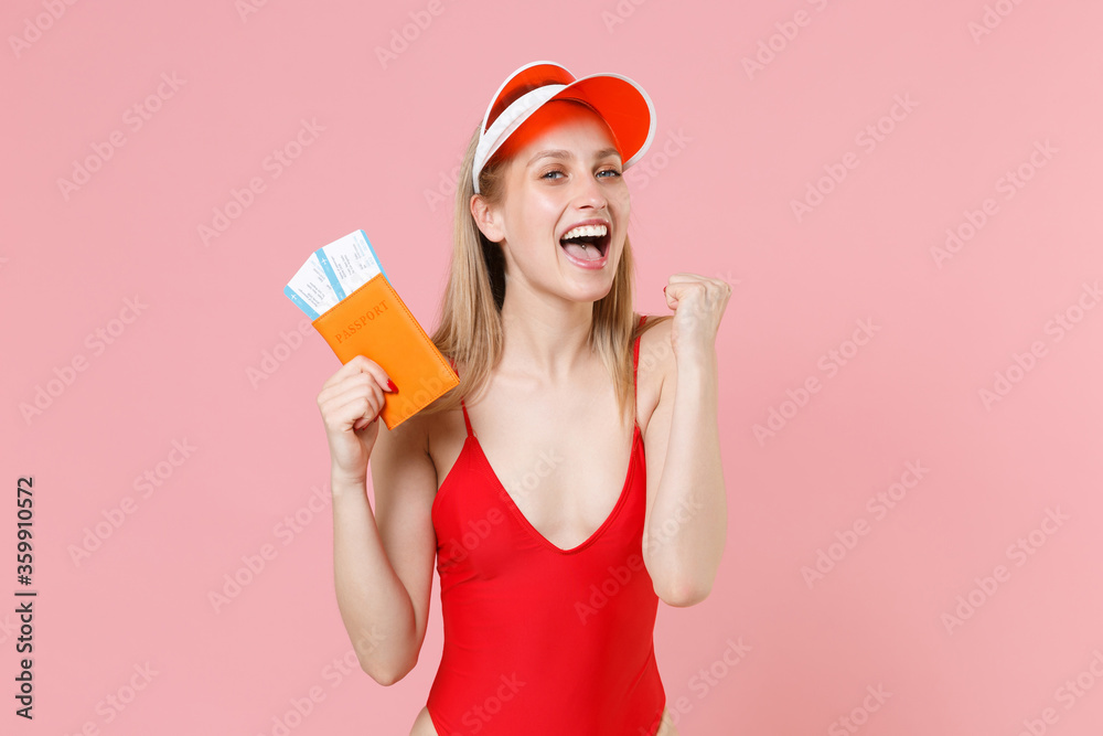 Happy blonde girl in red one-piece swimsuit cap isolated on pink background. People summer vacation rest lifestyle concept. Air flight journey. Hold passport ticket boarding pass doing winner gesture. Happy blonde girl in red one-piece swimsuit cap isolated on pink background. People summer vacation rest lifestyle concept. Air flight journey. Hold passport ticket boarding pass doing winner gesture.