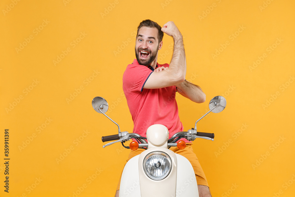 Excited young bearded guy in casual summer clothes driving moped isolated on yellow background studio portrait. Driving motorbike transportation concept. Mock up copy space. Showing biceps, muscles.