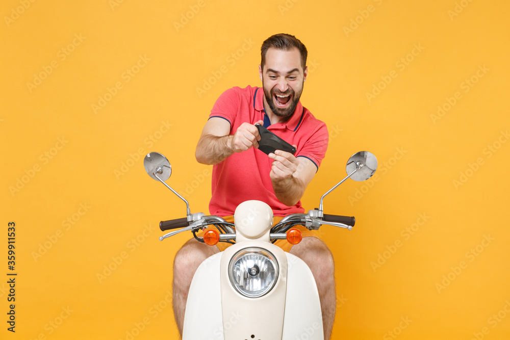 Cheerful young bearded man guy in summer clothes driving moped isolated on yellow background studio portrait. Driving motorbike transportation concept. Mock up copy space. Play game with mobile phone.