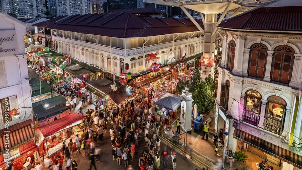TL/ZO/ Zoom Out Time lapse of busy night market during Chinese New Year in Singapore's Chinatown in front of the Singapore skyline, at dusk