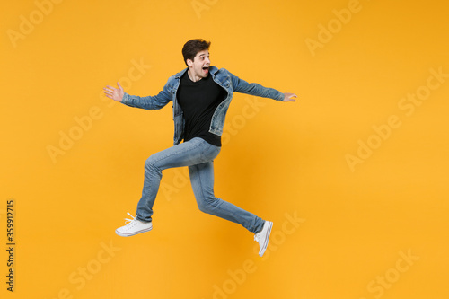 Excited young man guy 20s wearing casual denim clothes posing isolated on yellow background studio portrait. People emotions lifestyle concept. Mock up copy space. Jumping like running  looking aside.