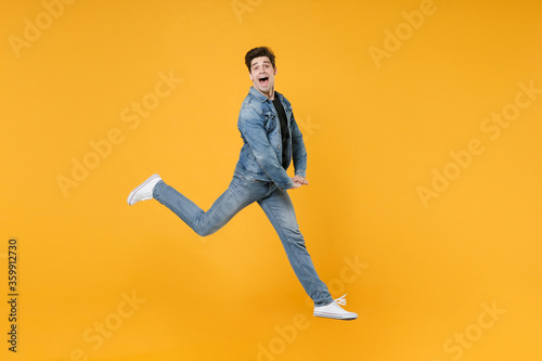Funny young man guy wearing casual denim clothes posing isolated on yellow background studio portrait. People emotions lifestyle concept. Mock up copy space. Jumping like dancing, spreading legs. © ViDi Studio