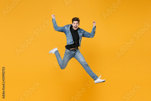 Excited young man guy wearing casual denim clothes posing isolated on yellow background studio portrait. People sincere emotions lifestyle concept. Mock up copy space. Jumping  doing winner gesture.