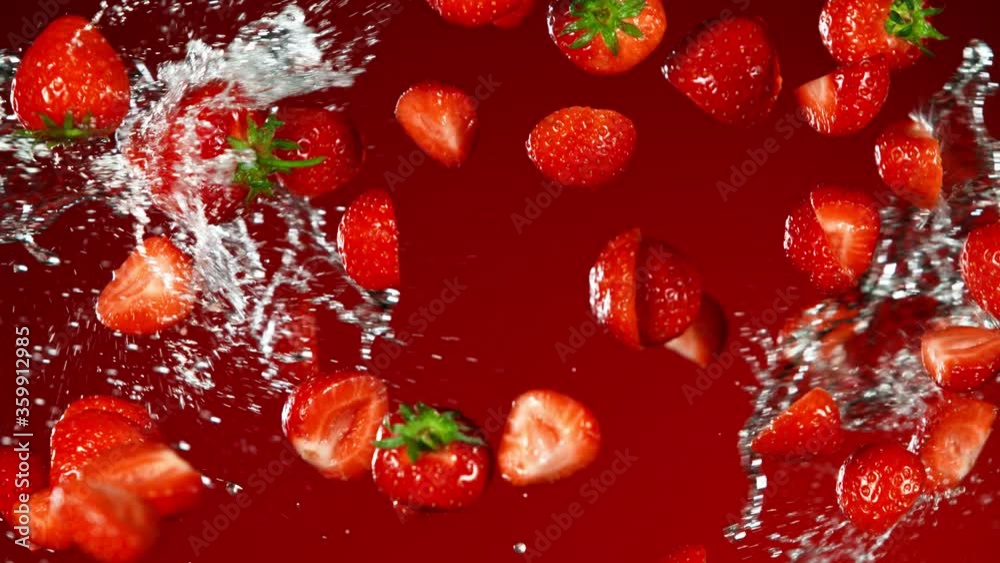Super Slow Motion Shot of Flying Fresh Strawberries and Water Side Splash on Red Background at 1000fps.
