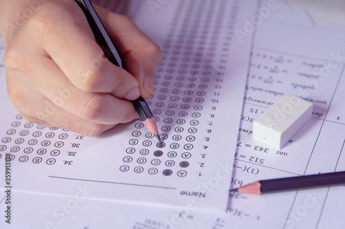 Students hand holding pencil writing selected choice on answer sheets and Mathematics question sheets. students testing doing examination. school exam.