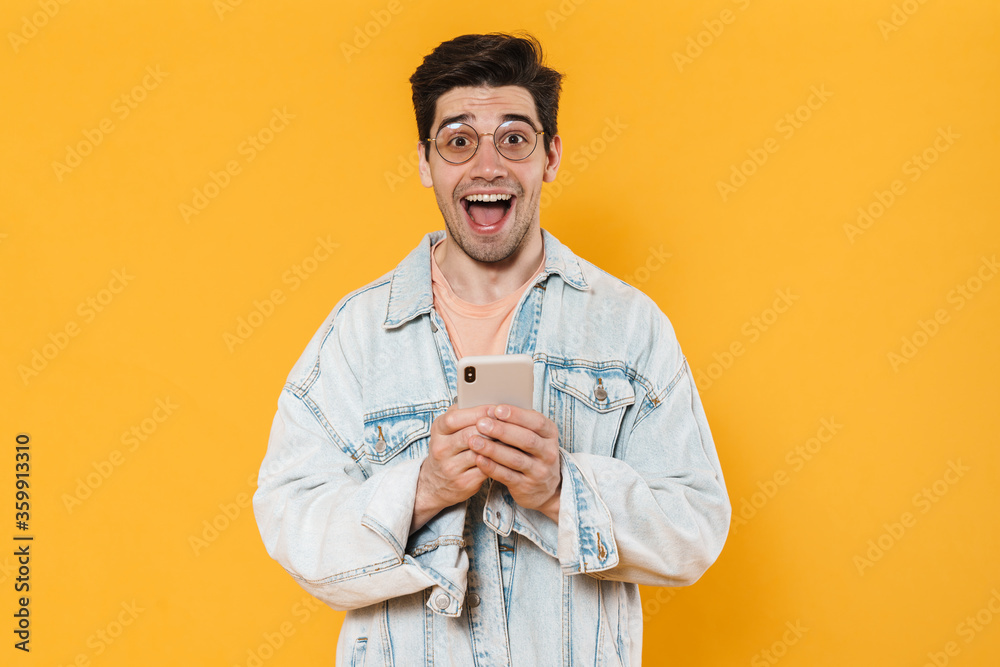 Photo of delighted young man screaming and using mobile phone