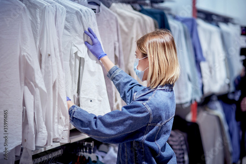 Safe shopping during an epidemic. A girl in a mask examines clothes in a store.