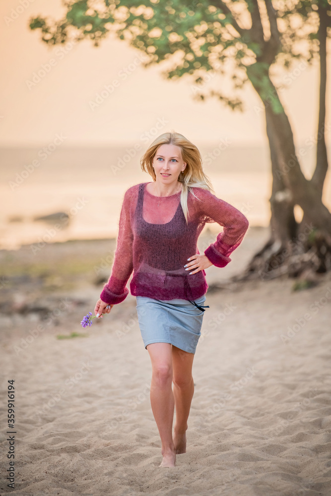 Women blonde outdoors walking on the sand towards the sea at sunset	
