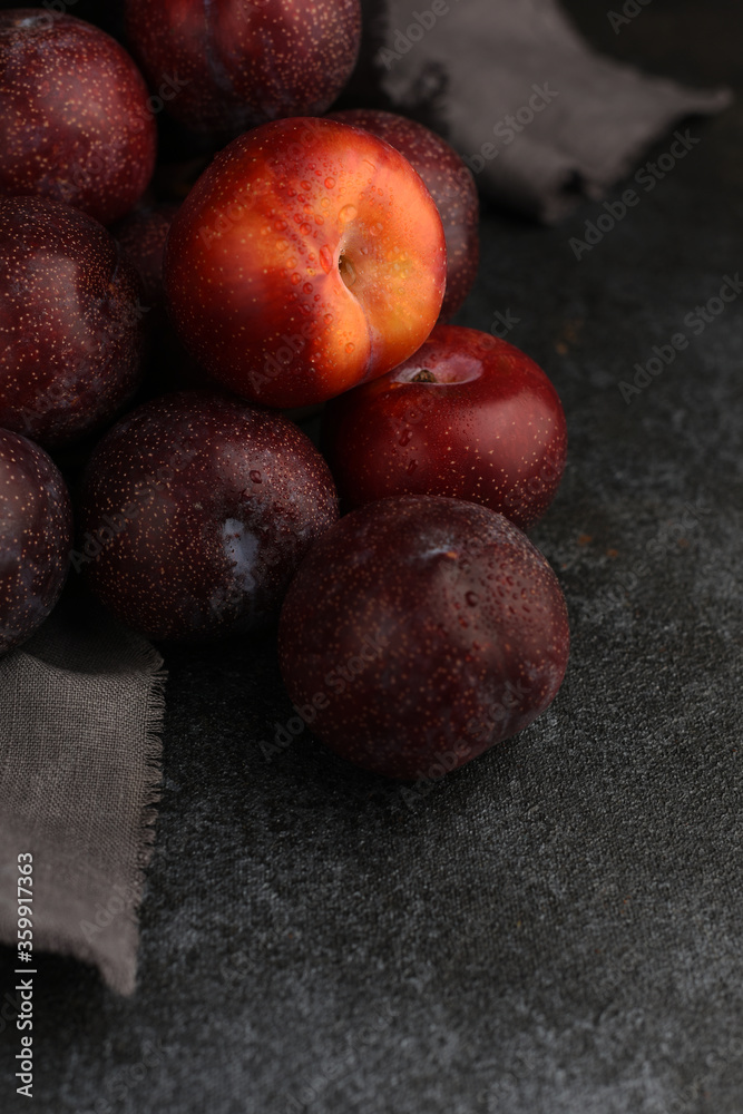 Plums on a dark stone textured background. Copy space. Blue plums natural fruit background. Selective focus. Red ripe plum above blue plums. Plums on a dark stone textured background. Copy space. Blue plums natural fruit background. Selective focus. Red ripe plum above blue plums.