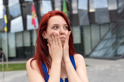 Portrait Screaming woman on street near mall happy and surprised hold their cheeks by hand. Beautiful girl with red hair pointing to looking right. Expressive facial expressions of an entrepreneur.