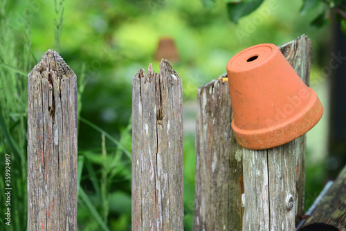 Detail of an old weathered wooden fence over which a clay flower pot is placed in the garden