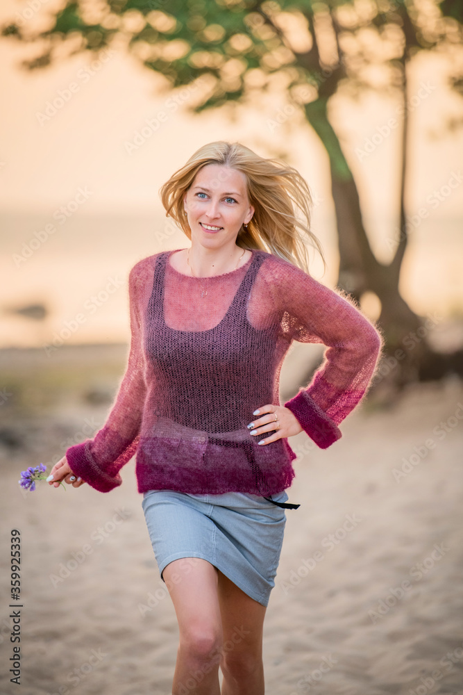 Women blonde outdoors walking on the sand towards the sea at sunset Women blonde outdoors walking on the sand towards the sea at sunset