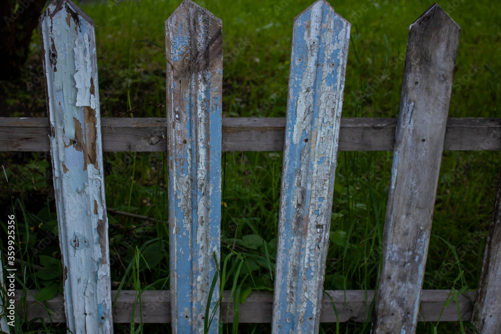 Old dilapidated wooden fence with paint on the background of green grass. The concept of simple rural life. Village background. Old dilapidated wooden fence with paint on the background of green grass. The concept of simple rural life. Village background.