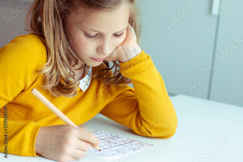 Portrait of dorable teen girl solving sudoku at desk at school or at home. View from above