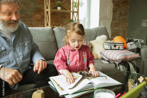 Grandfather and grandchild playing together at home. Happiness, family, relathionship, learning and education concept. Sincere emotions and childhood. Reading books, fairytails, poems, look happy. photo