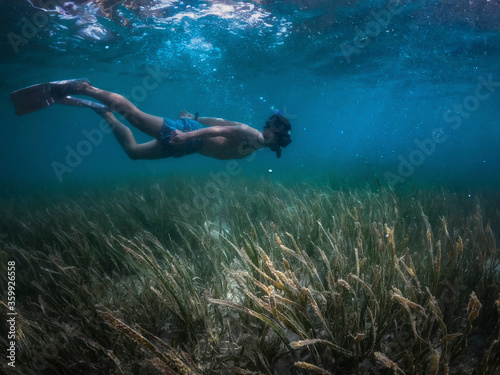 Side view of man free diving under the dark sea with coral and reef.