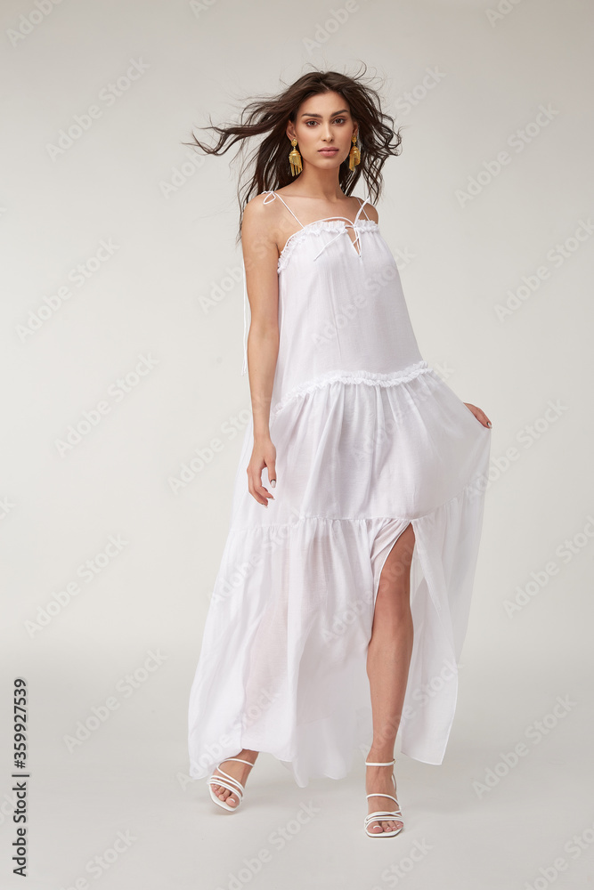 Beautiful woman fashion model makeup brunette hair perfect body shape tanned skin wear clothes summer collection organic long white silk dress stylish sandals shoes, accessory jewelry earrings date.