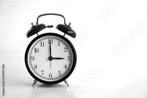 Black vintage alarm clock on table. White background. An image of a retro clock showing 03:00 pm/am.