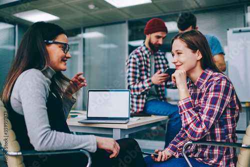 Successful male and female colleagues communicating with each other during working process in office.Young women laughing during friendly conversation sitting at table with laptop with blank screen