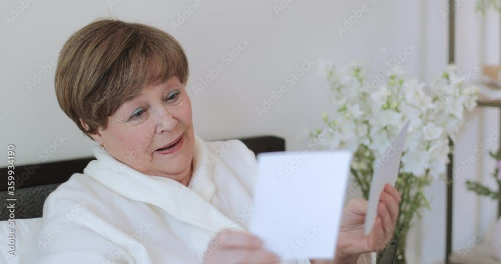 Close up view of beautiful grandmother in good mood looking at photos and smiling. Good looking woman in 60s having nostalgia while going through old pictures. Concept of memories. Close up view of beautiful grandmother in good mood looking at photos and smiling. Good looking woman in 60s having nostalgia while going through old pictures. Concept of memories.