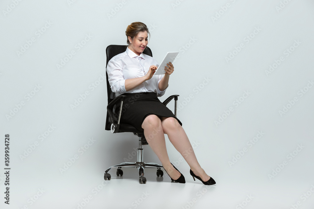 Gadgets. Young woman in office attire. Bodypositive female character, feminism, loving herself, beauty concept. Plus size businesswoman on gray background. Boss, beautiful. Inclusion, diversity. Gadgets. Young woman in office attire. Bodypositive female character, feminism, loving herself, beauty concept. Plus size businesswoman on gray background. Boss, beautiful. Inclusion, diversity.