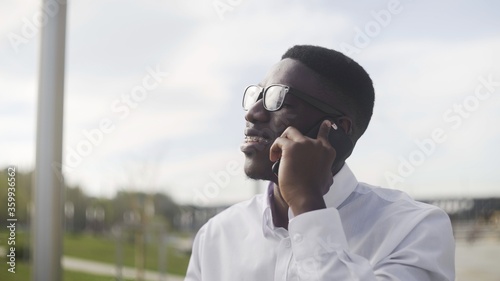 Young African Businessman with braces talking on cell phone in city park © stanis88