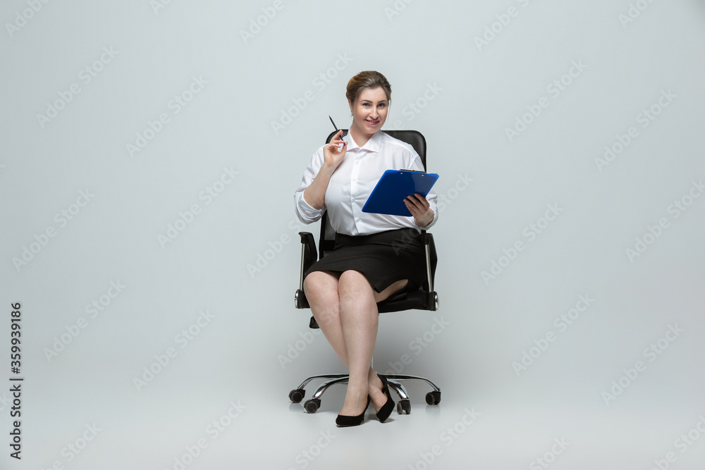 Naklejka premium Meeting. Young woman in office attire. Bodypositive female character, feminism, loving herself, beauty concept. Plus size businesswoman on gray background. Boss, beautiful. Inclusion, diversity.