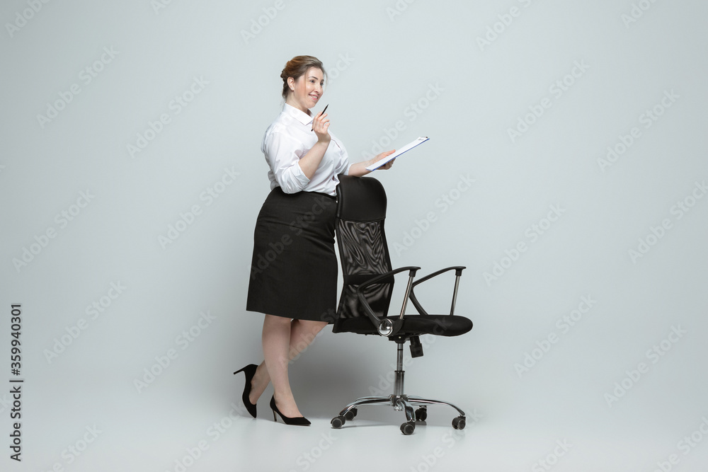 Meeting. Young woman in office attire. Bodypositive female character, feminism, loving herself, beauty concept. Plus size businesswoman on gray background. Boss, beautiful. Inclusion, diversity.