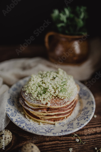 Tasty pancakes with icing sugar and flowers on a vintage plate. Rustic background with breakfast.