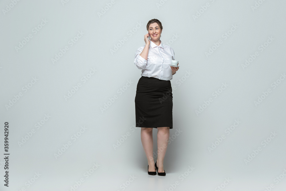 Coffee break. Young woman in office attire. Bodypositive female character, feminism, loving herself, beauty concept. Plus size businesswoman on gray background. Boss, beautiful. Inclusion, diversity. Coffee break. Young woman in office attire. Bodypositive female character, feminism, loving herself, beauty concept. Plus size businesswoman on gray background. Boss, beautiful. Inclusion, diversity.