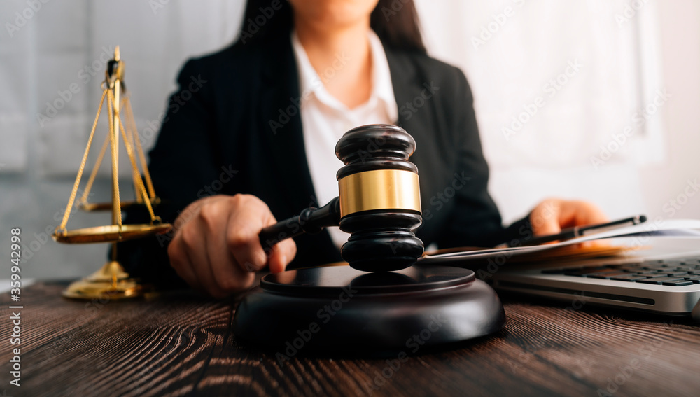 Justice and law concept.Male judge in a courtroom with the gavel, working with, computer and docking keyboard, eyeglasses, on table in morning light Justice and law concept.Male judge in a courtroom with the gavel, working with, computer and docking keyboard, eyeglasses, on table in morning light