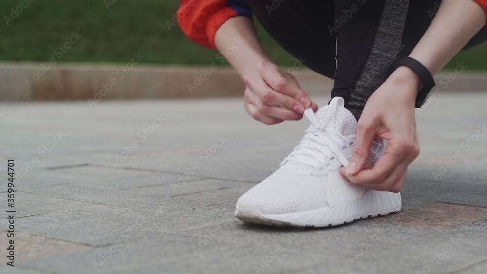 Female Athlete ties up shoelaces, white sneakers, white socks, in sports clothes, runs on the street.
