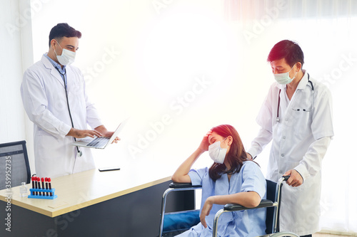 A patient woman wear face mask and sitting on wheelchair and covid-19 emergency treatment in a hospital room  doctors wear uniform protection