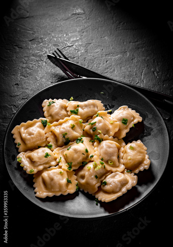 Meat dumplings - russian pelmeni, ravioli with meat in black plate on Dark grey black slate background